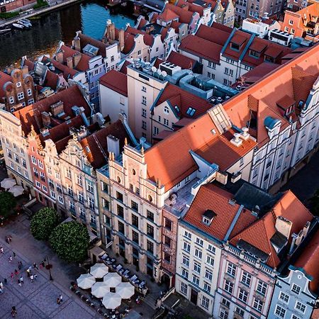 فندق راديسون بلو، غدانسك المظهر الخارجي الصورة The photo shows a bird's-eye view of a picturesque urban area, likely in a historical city. It features a cluster of buildings with a mix of architectural styles, characterized by colorful facades and predominantly red rooftops. The buildings seem to