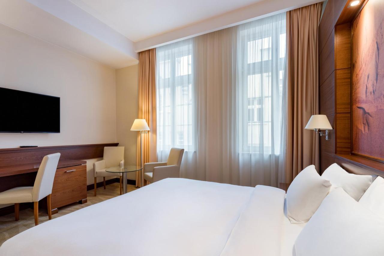 فندق راديسون بلو، غدانسك المظهر الخارجي الصورة The photo depicts a modern hotel room. It features a neatly made bed with white linens, flanked by two pillows. On the wall opposite the bed, there is a flat-screen television mounted. There are two windows with sheer curtains that allow natural ligh