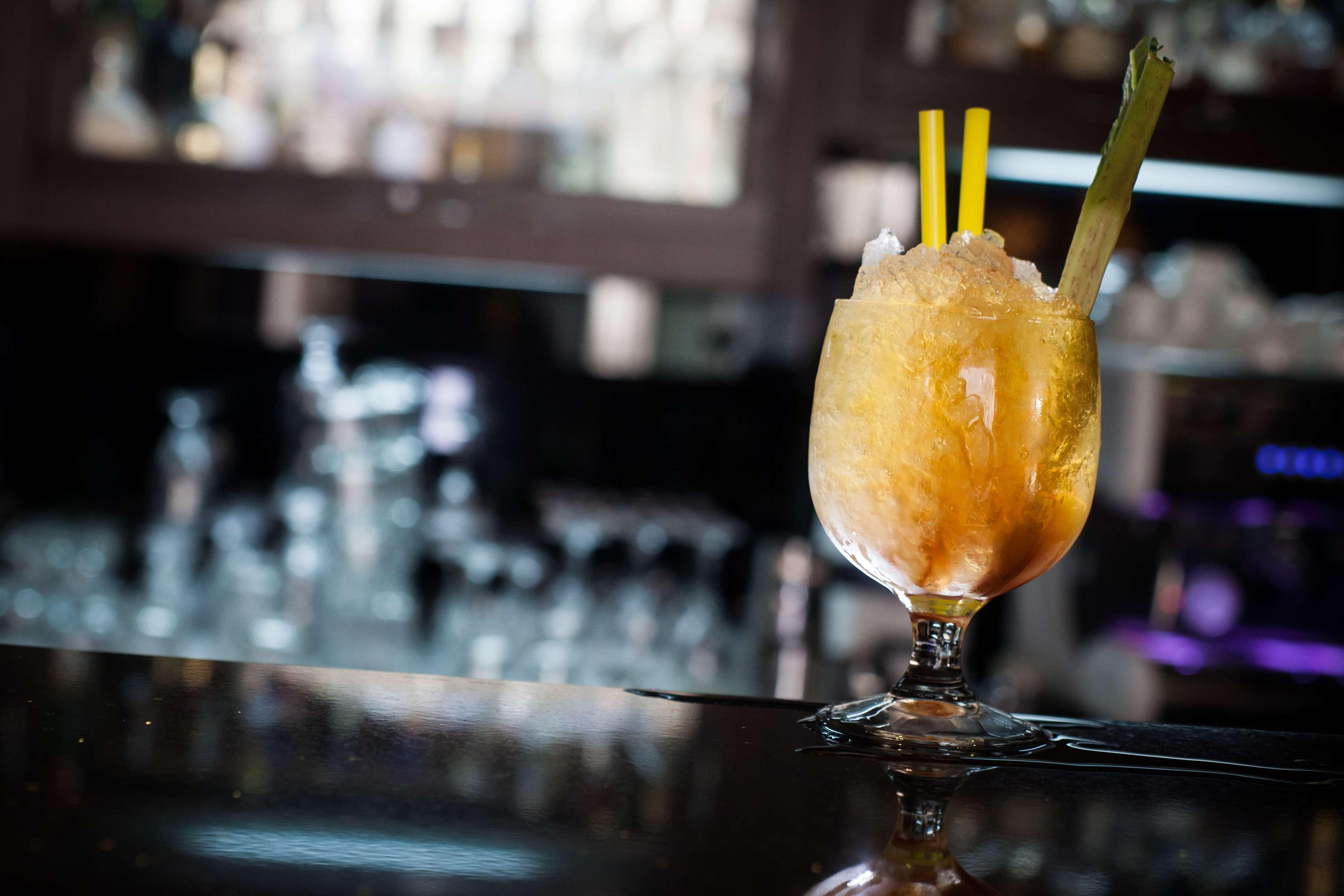 فندق راديسون بلو، غدانسك المظهر الخارجي الصورة The photo shows a cocktail served in a decorative glass. The drink appears to be slushy or frozen, with a yellow-orange hue and topped with crushed ice. It has two yellow straws and a piece of celery as garnish. The setting suggests it is in a bar or