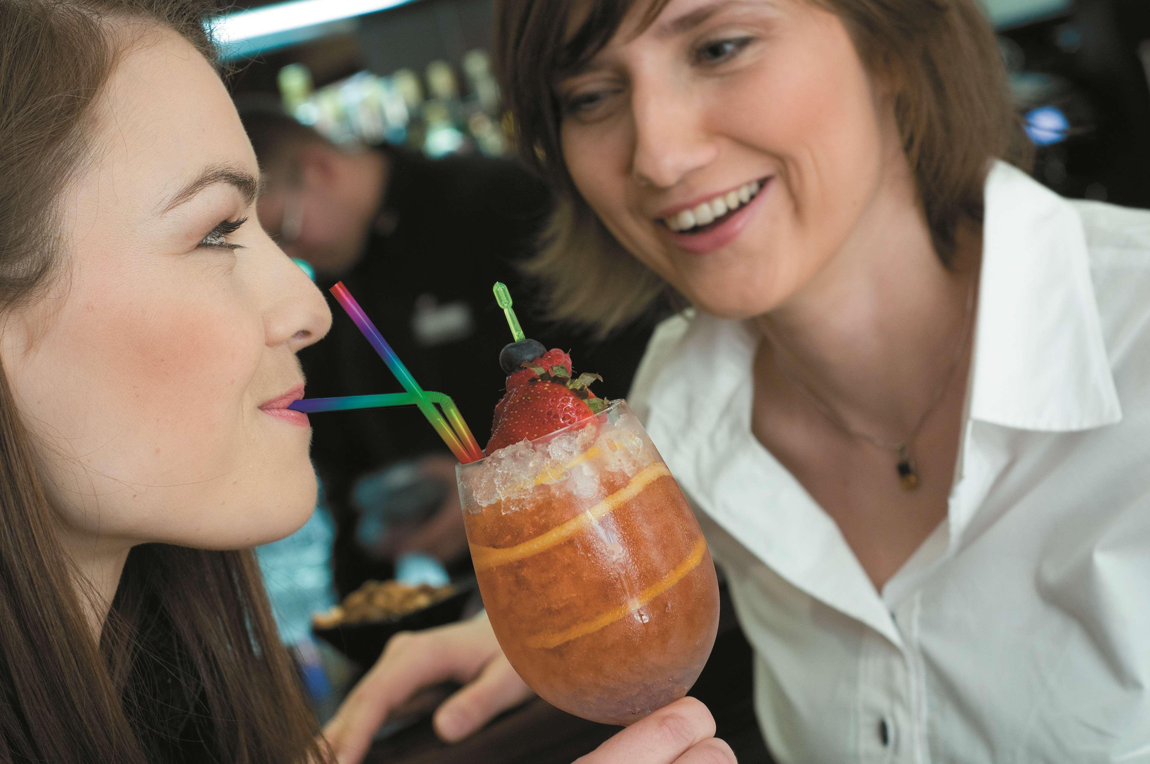فندق راديسون بلو، غدانسك المظهر الخارجي الصورة The photo shows two women engaging with each other, smiling and enjoying a moment together. One woman is holding a colorful drink in a large glass adorned with ice, fruit, and multiple straws. The other woman looks on with a friendly expression, cont