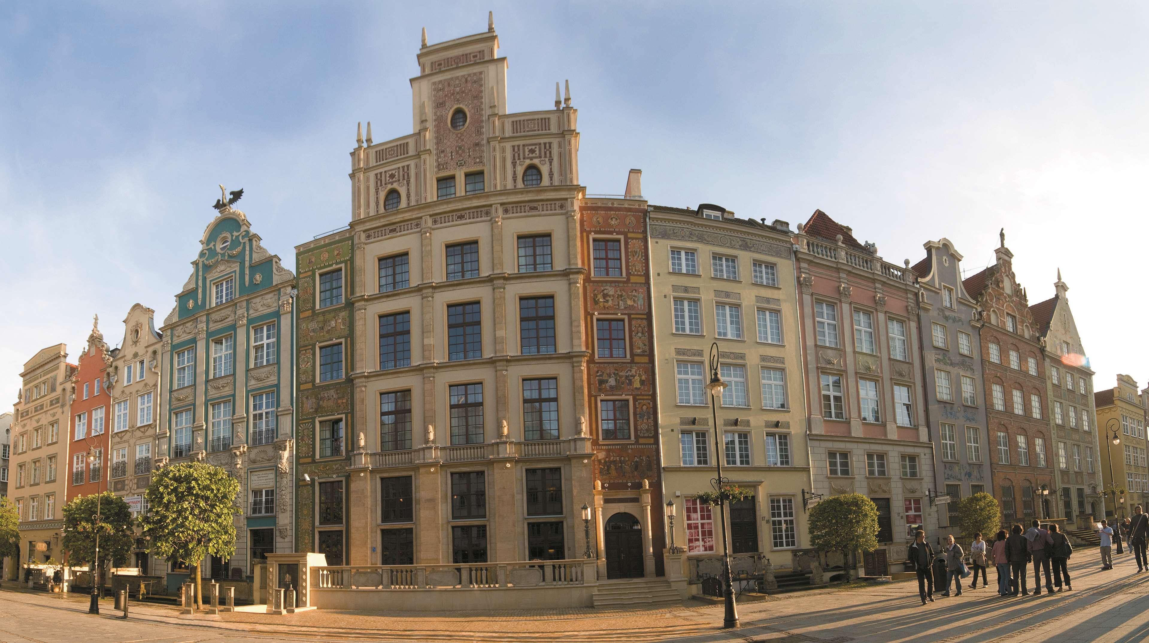فندق راديسون بلو، غدانسك المظهر الخارجي الصورة The photo showcases a panoramic view of a row of historic buildings, likely in a European city. The architecture features a blend of styles, presenting a vibrant facade with multiple colors and decorative elements. Each building has distinct characte
