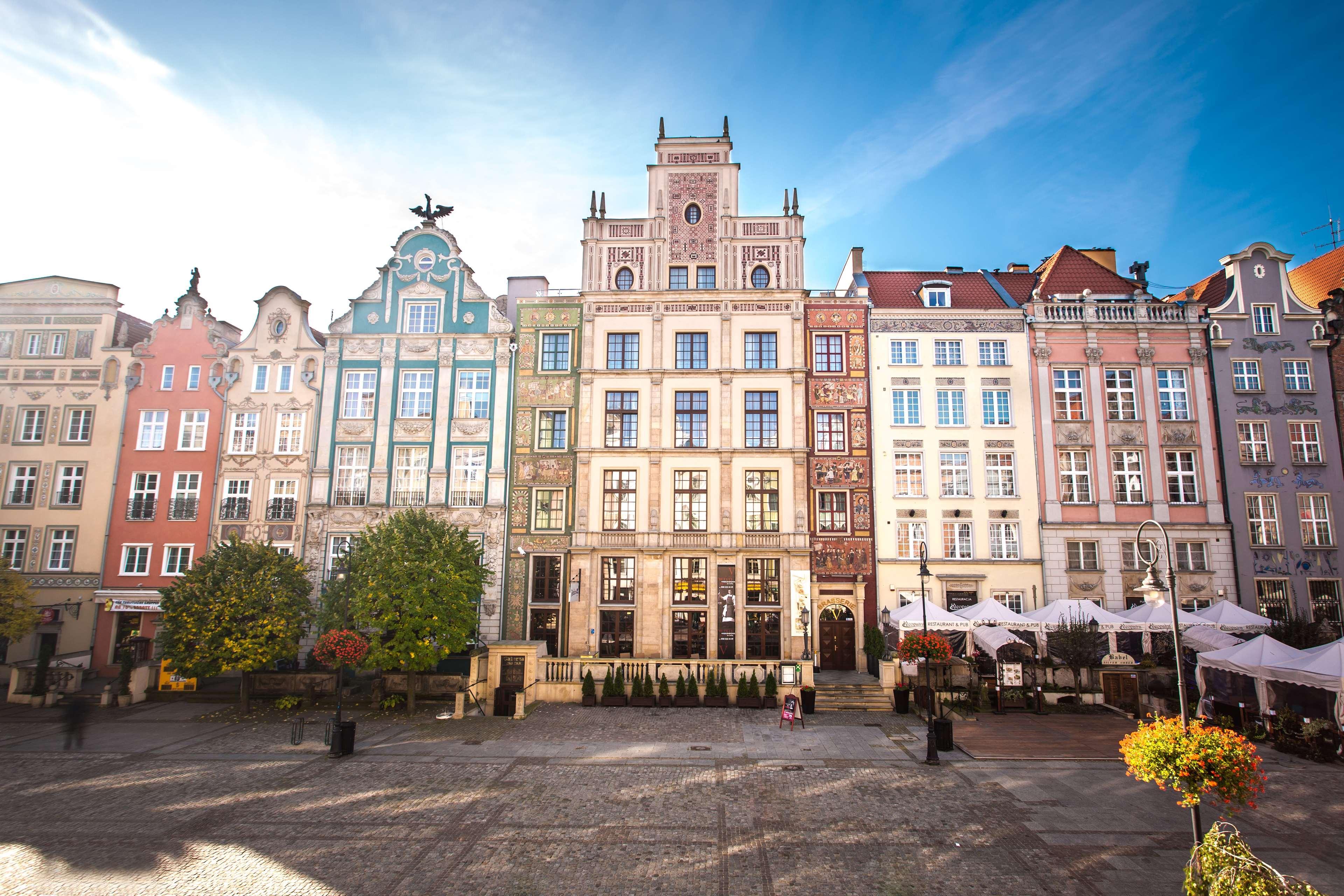 فندق راديسون بلو، غدانسك المظهر الخارجي الصورة The photo depicts a picturesque square in a historic European city, likely Gdańsk, Poland. The scene features an array of colorful, well-preserved buildings with ornate architectural details. These buildings are characterized by vibrant facades in va