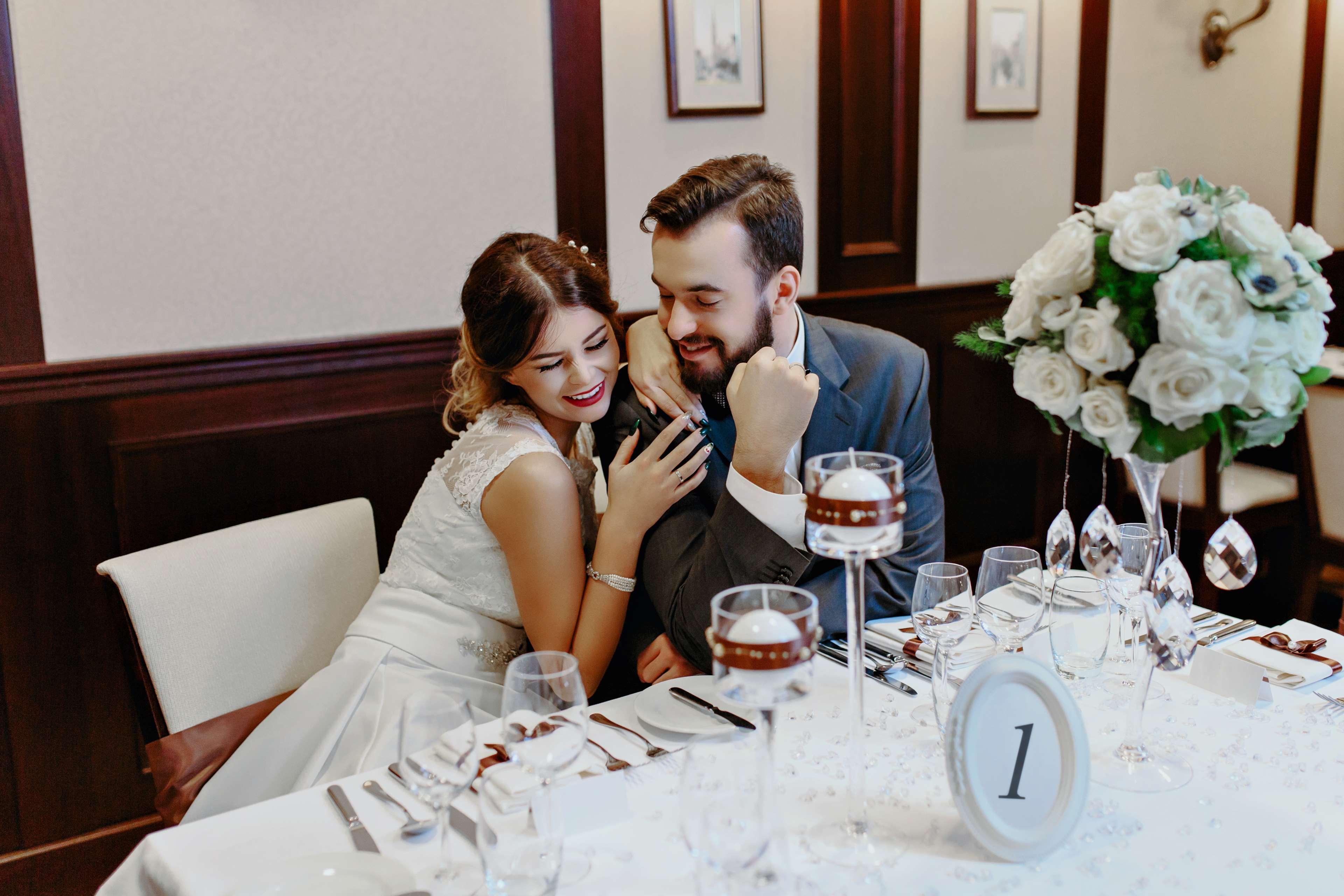فندق راديسون بلو، غدانسك المظهر الخارجي الصورة The photo depicts a couple sitting at a beautifully arranged dining table. The woman, dressed in a white wedding gown, leans affectionately towards the man, who is wearing a gray suit. They appear to be enjoying a moment together, smiling and engagin