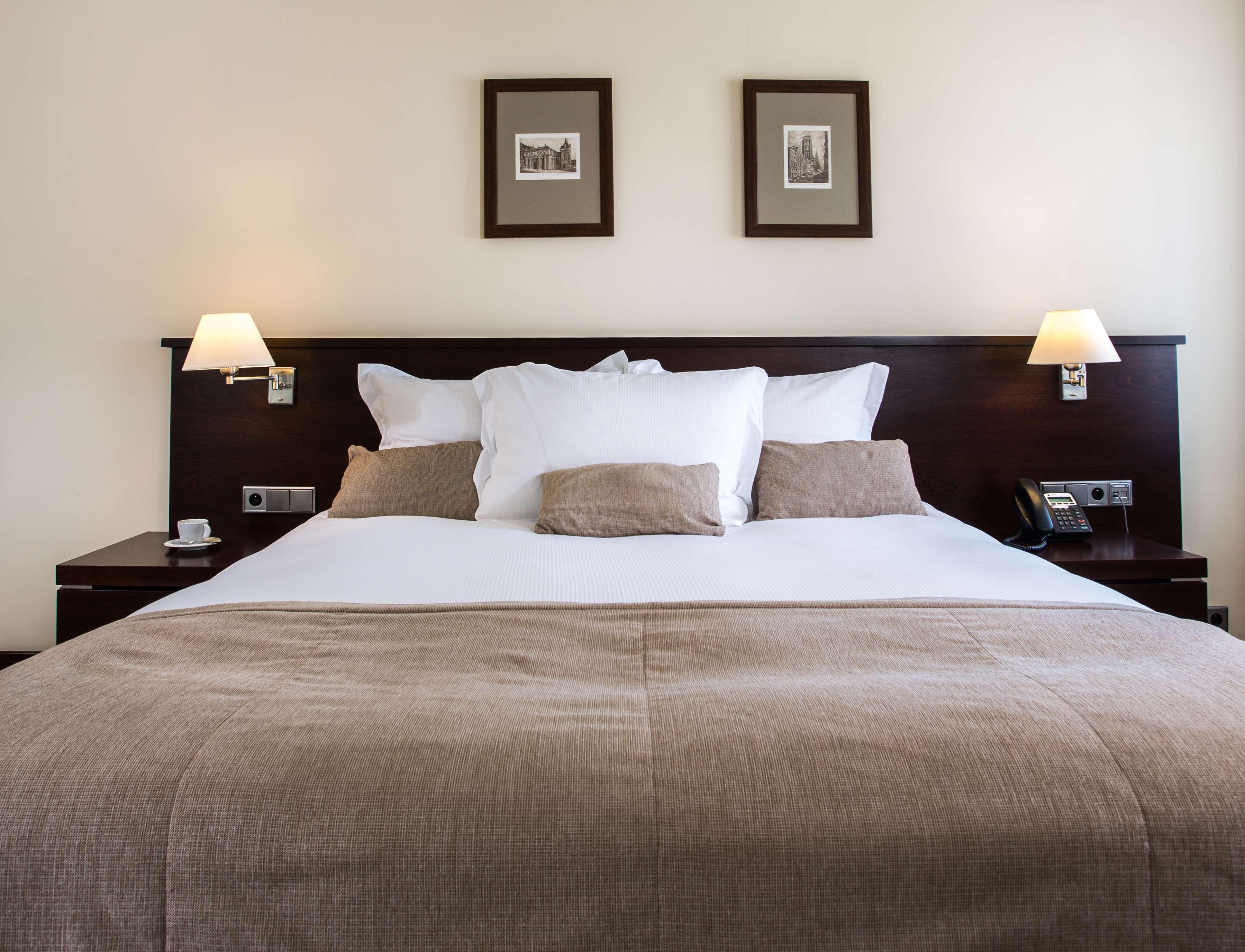 فندق راديسون بلو، غدانسك المظهر الخارجي الصورة The photo shows a well-decorated hotel room, focusing on a large bed with a dark wood headboard. The bed is adorned with several white pillows and a couple of beige cushions. There are two lamps on either side of the bed, providing soft lighting. Abo