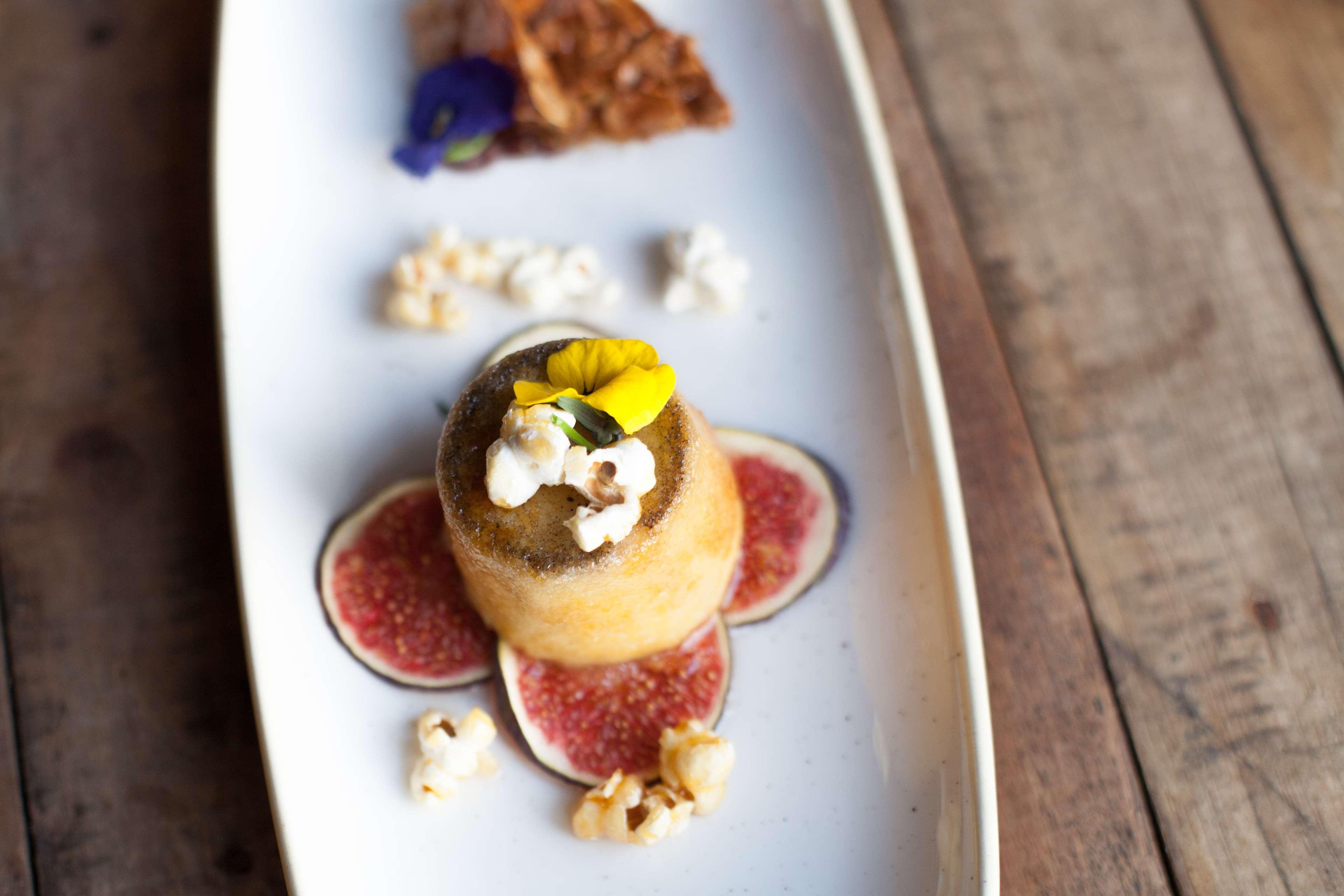 فندق راديسون بلو، غدانسك المظهر الخارجي الصورة The photo features an elegantly presented dessert on a white plate. In the center, there is a small dome-shaped cake topped with a yellow flower and popcorn. Surrounding it are slices of fig and scattered popcorn. To the side, there is a piece of a c