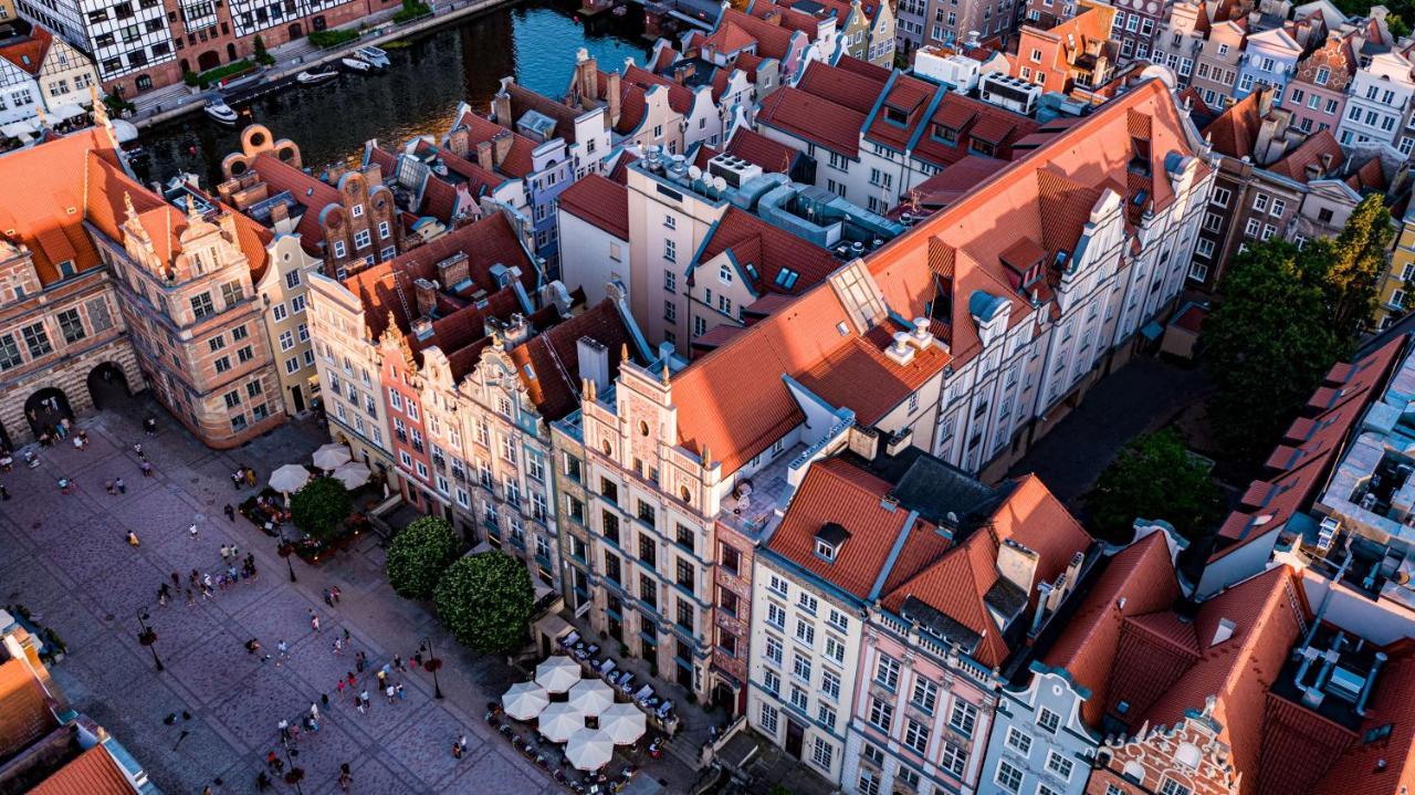 فندق راديسون بلو، غدانسك المظهر الخارجي الصورة The photo shows a bird's-eye view of a picturesque urban area, likely in a historical city. It features a cluster of buildings with a mix of architectural styles, characterized by colorful facades and predominantly red rooftops. The buildings seem to