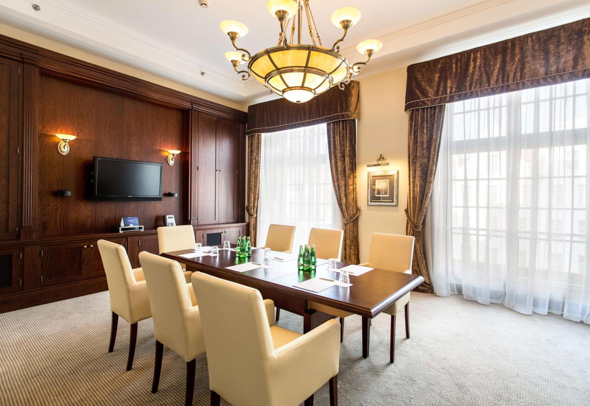 فندق راديسون بلو، غدانسك المظهر الخارجي الصورة The photo shows a well-furnished conference room. It features a large wooden table surrounded by six cream-colored chairs. On the table, there are several green glass bottles of water. The room is well-lit with a decorative chandelier hanging from th
