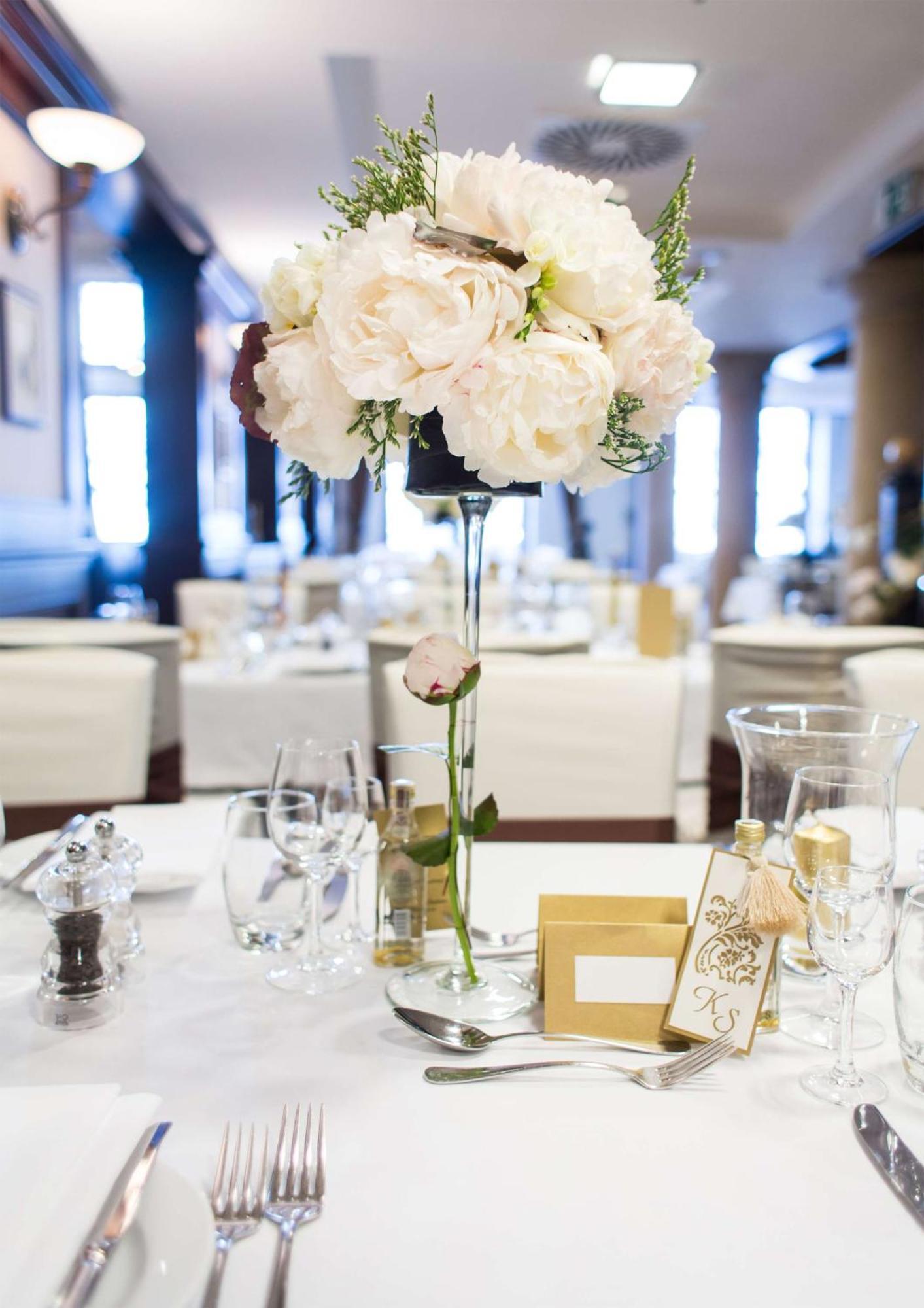 فندق راديسون بلو، غدانسك المظهر الخارجي الصورة The photo depicts a beautifully arranged table setting, likely for a formal event or celebration. At the center of the table is a tall floral arrangement featuring soft pink peonies and greenery, elegantly placed in a clear vase. Surrounding the cent