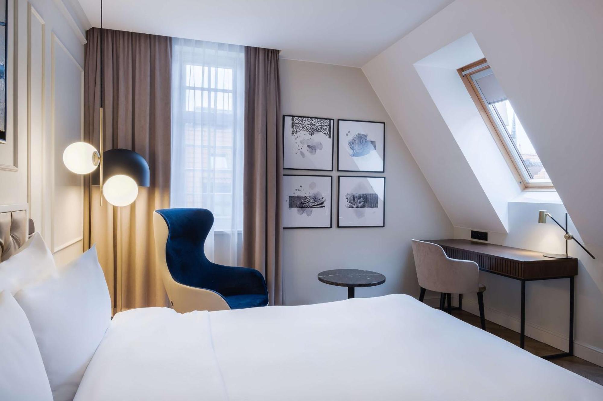 فندق راديسون بلو، غدانسك المظهر الخارجي الصورة The photo shows a cozy hotel room featuring a modern design. The room has a double bed with a white duvet, and a large window with sheer curtains that allows natural light to filter in. On the wall opposite the bed, there are several framed artworks.