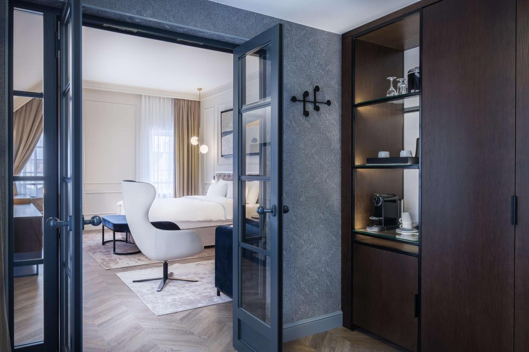 فندق راديسون بلو، غدانسك المظهر الخارجي الصورة The photo shows a luxuriously designed hotel room viewed from an entrance. In the foreground, there is a doorway with dark double doors leading into the main area. To the right, there is a wooden cabinet with shelves displaying some items, including 