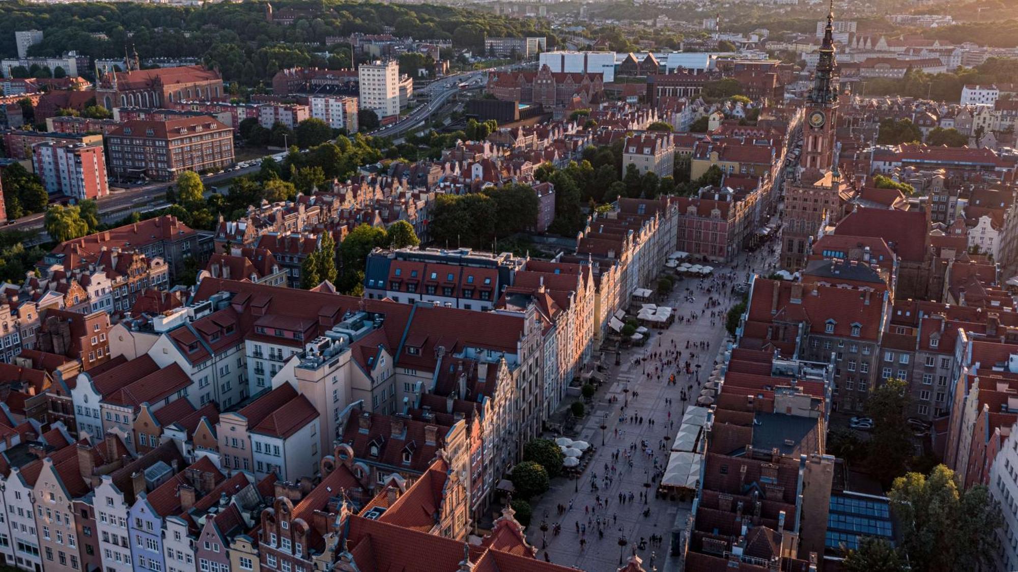 فندق راديسون بلو، غدانسك المظهر الخارجي الصورة The photo depicts a scenic aerial view of a city, likely Gdańsk in Poland. The landscape features historical buildings with distinctive architecture, characterized by colorful facades and prominent rooftop designs. A bustling street runs through the 